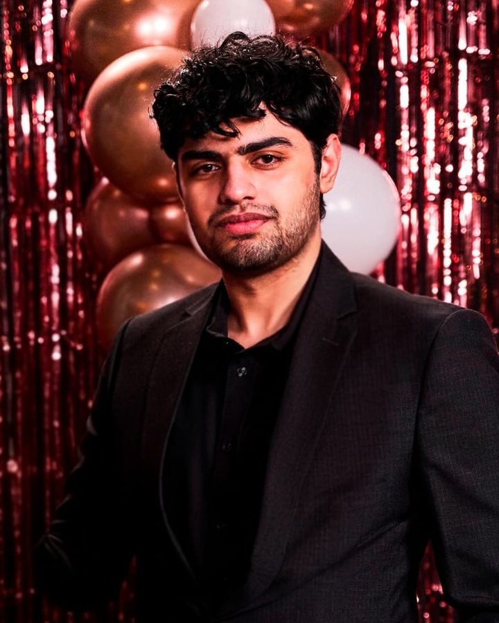 Saad Tariq in a dark suit at an event, in front of balloons and a glitter curtain